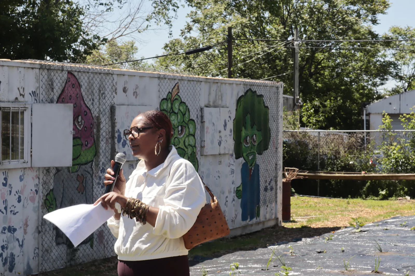 A community leader speaking beside a youth-painted garden mural
